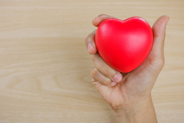 Red heart on hand on wooden background.