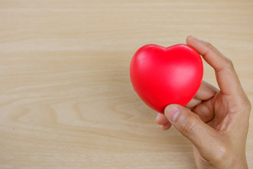 Red heart on hand on wooden background.