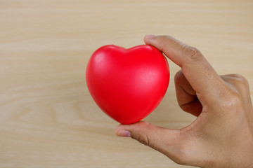 Red heart on hand on wooden background.