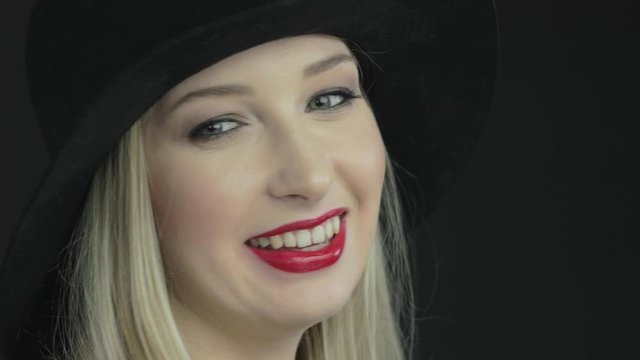 Young blonde fashion model wearing a large black hat smiles and winks at the camera.