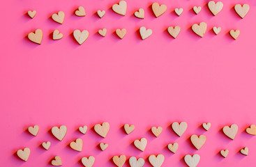 Many small wooden hearts on a pink background and copy space.