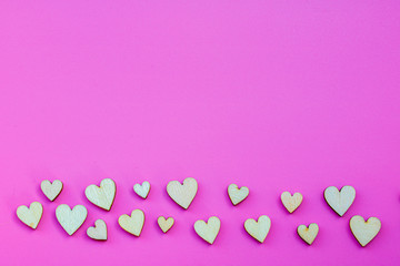 Many small wooden hearts on a pink background and copy space.