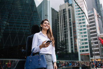 Laughing formal female worker surfing smartphone on street