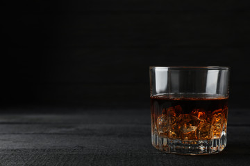 Glass of whiskey with ice cubes on dark wooden background, space for text