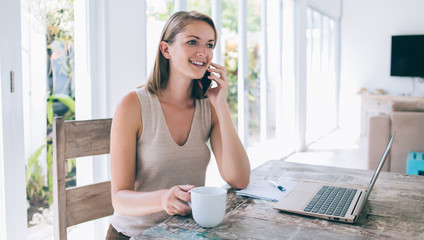 Delighted female sitting at desk and chatting by mobile