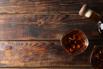 Bottle and glasses of whiskey on wooden background, top view