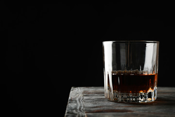 Glass of whiskey on wooden background, space for text