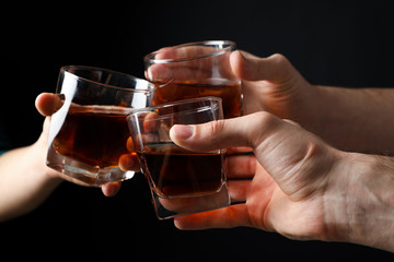 Three male hands holds glasses of whiskey on black background, close up. Cheers