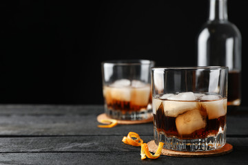 Glasses of whiskey with orange peels and ice on wooden background with bottle, space for textGlasses of whiskey with orange peels and ice on wooden background with bottle, space for text