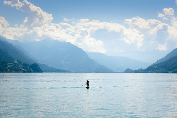 Silhouette of a man standing on a paddleboard on Lake Brienz in Switzerland. Hills in the background. Active lifestyle, sport activities. Peaceful background, motivational concept