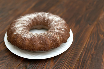 round chocolate cake sprinkled with powdered sugar on a wooden background