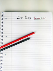 New Year resolution written on a blank sheet of paper in a notebook with pens placed on top, ready for new achievements and New Year