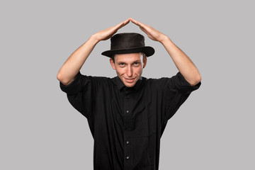 Stylish handsome man a black shirt and pork pie hat holding hands in a shape of a roof