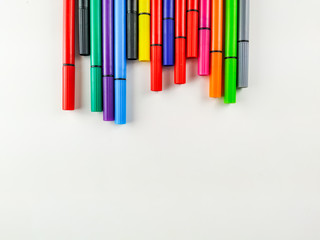 Colorful pens with caps on white background on upper side of the image making an interesting frame for studying, back to school, note taking etc