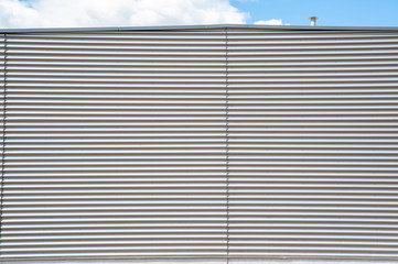 Fototapeta premium Grey wall of indistrial building, made of corrugated metal. Sunny day with blue sky.
