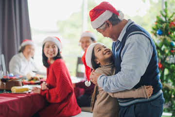 Big Asian family celebration in Christmas day, grandfather hug and looking at granddaughter in front of meal table of family which smiling and felling happy at home. Merry Xmas and happy new year.
