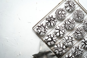 Chocolate crinkle cookies with powdered sugar icing. Cracked chocolate biscuits on an iron lattice on a light background top view copy space