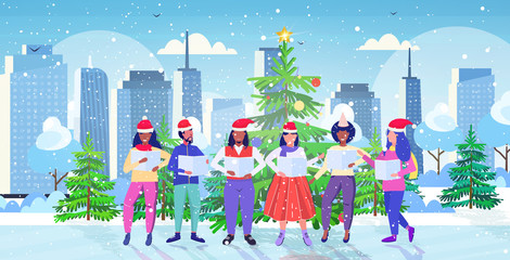 people with sheet books giving performance merry christmas happy new year holidays celebration concept mix race men women standing near fir tree modern cityscape background full length horizontal