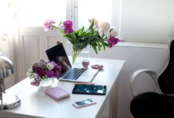 Female office desk workspace homeoffice mock up with laptop, pink peony flowers bouquet, smartphone, pink accessories and pink cup of coffee. Fashion, beauty or lifestyle blog concept.