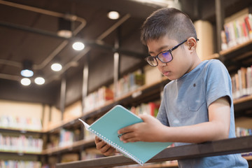 Asian boy student standing and reading a book at the library in the school.Students search for books in the bookshelf.Portrait Asian boy.