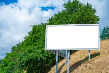 Blank white advertising billboard on the hillside in the city. Sunny summer day with blue sky.