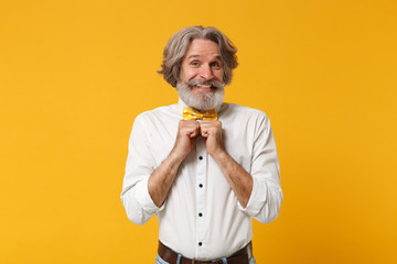 Smiling Elderly gray-haired mustache bearded man in white shirt bow tie posing isolated on yellow orange wall background studio portrait. People lifestyle concept. Mock up copy space. Clenching fists.