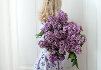 Blonde hair woman in dress posing with bouquet of lilac flowers over white background. Lilac flower in a female hands.