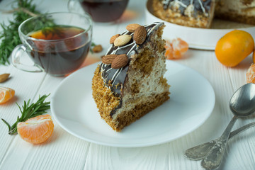 Chocolate cake with almonds on a white plate on the table on a light wooden background. Tea party with cake. Dining table.