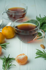 Tea in a glass cup on a light wooden background. Black tea with rosemary and tangerines. Space for text.