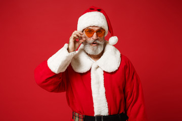 Elderly gray-haired bearded Santa man in Christmas hat, sunglasses posing isolated on red background in studio. Happy New Year 2020 celebration holiday concept. Mock up copy space. Styling mustache.