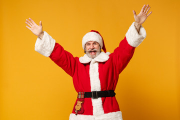 Fototapeta na wymiar Joyful elderly gray-haired mustache bearded Santa man in Christmas hat posing isolated on yellow wall background. Happy New Year 2020 celebration holiday concept. Mock up copy space. Rising hands.