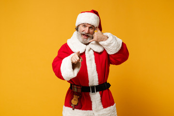 Fototapeta na wymiar Elderly gray-haired mustache bearded Santa man in Christmas hat isolated on yellow background. Happy New Year 2020 celebration concept. Mock up copy space. Doing phone gesture like says call me back.