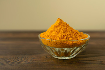 Turmeric powder in glass bowl at wooden background.
