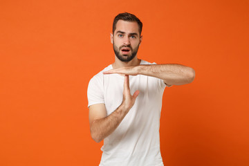 Perplexed young man in casual white t-shirt posing isolated on orange wall background, studio portrait. People sincere emotions lifestyle concept. Mock up copy space. Holding hands perpendicularly.