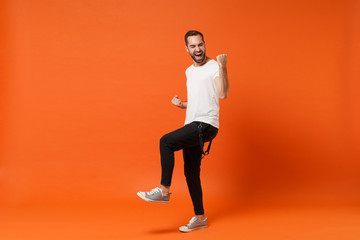 Fototapeta na wymiar Overjoyed happy young man in casual white t-shirt posing isolated on bright orange wall background studio portrait. People sincere emotions lifestyle concept. Mock up copy space. Doing winner gesture.