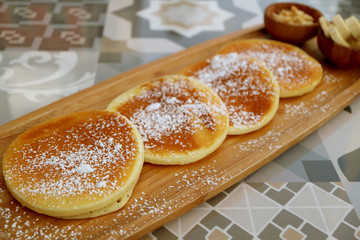Pancakes with icing sugar on wooden plate served on patterned stone table 