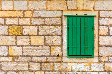 The facade of an old stone house with a window with green shutters. Croatia