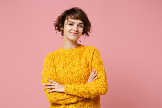 Smiling young brunette woman girl in yellow sweater posing isolated on pastel pink background studio portrait. People sincere emotions lifestyle concept. Mock up copy space. Holding hands crossed.