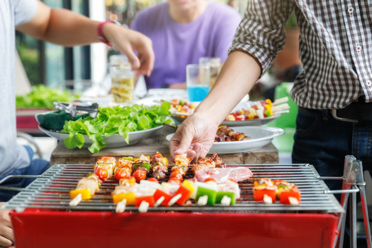 A Man Grilling Pork And Barbecue In Dinner Party. Food, People And Family Time Concept.