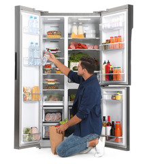 Man with bag of groceries near open refrigerator on white background