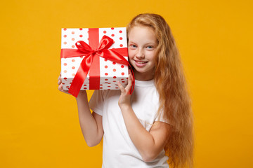 Smiling little ginger kid girl 12-13 years old in white t-shirt isolated on yellow background. New Year Women's Day birthday holiday concept. Mock up copy space. Hold present box with gift ribbon bow.