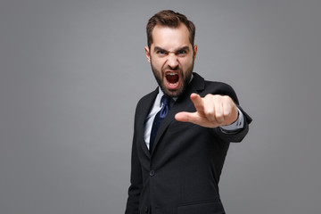 Angry young bearded business man in suit shirt tie posing isolated on grey background. Achievement career wealth business concept. Mock up copy space. Point index finger on camera, screaming swearing.