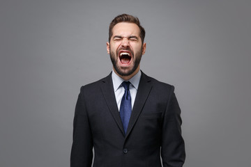 Frustrated young business man in classic black suit shirt tie posing isolated on grey wall background. Achievement career wealth business concept. Mock up copy space. Keeping eyes closed, screaming.