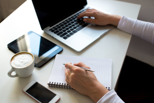 Horizontal view image of woman's hands using and typing on laptop with coffee cup, notebook, tablet in white colors on table. Business woman, feminine, business background