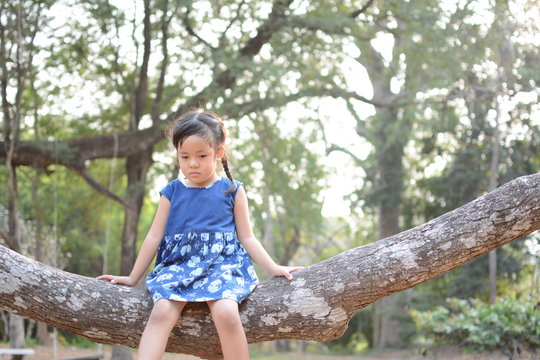 Asian child girl angry and sad. she sitting on the branch of tree over nature background.