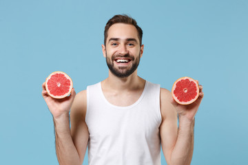 Bearded young man 20s years old in white shirt hold in hand half of grapefruit isolated on blue...