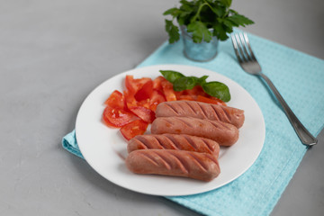 Breakfast of sausages and vegetables. Tomato sliced. On a light background.