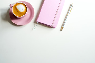 Pink notebook and cup of cappuccino coffee with pink tulips on white background. Pink writing set with cappuccino. Woman's workplace in pink. Flat lay. Top view. Copy space