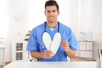 Fototapeta premium Handsome male orthopedist showing insoles in clinic