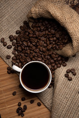 Cup of coffee and coffee beans in a tourniquet bag on the table. View from above.